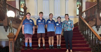 4 children and their teacher standing on the stairs inside Parliament House