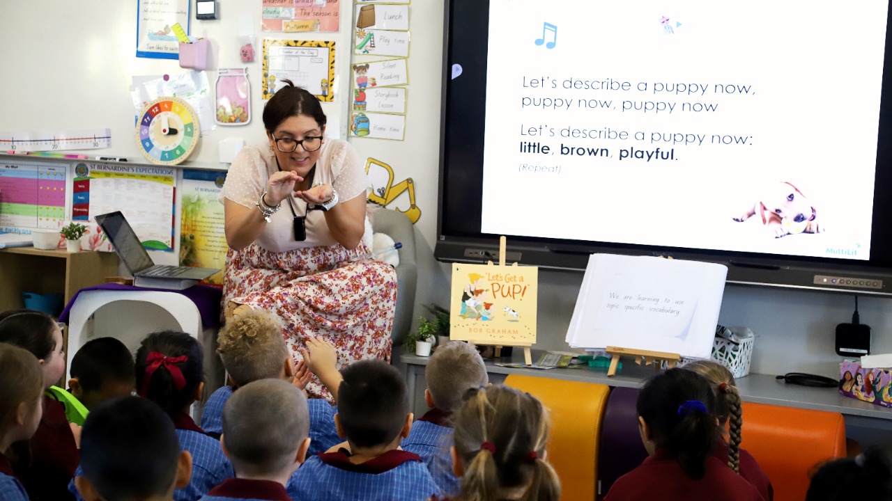 Teacher leading a group reading and language activity with early years students, highlighting interactive learning, vocabulary development and engagement through shared storytelling