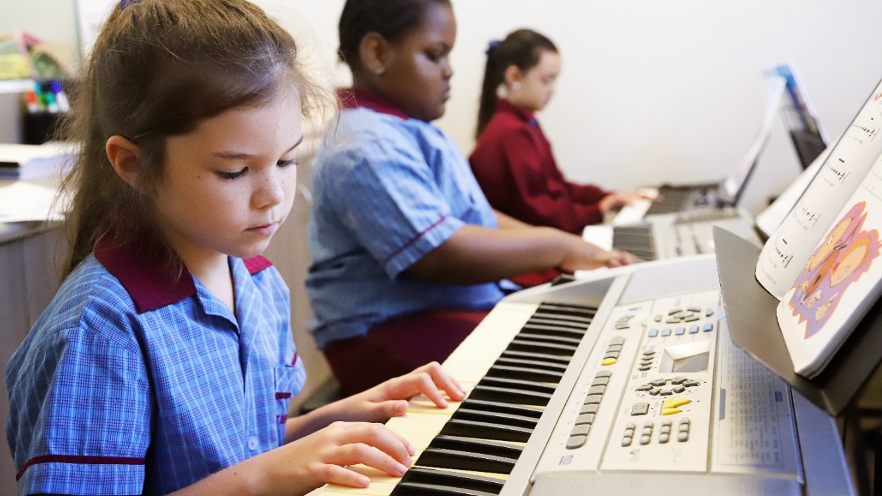 Students playing keyboards during a music lesson, highlighting music education, concentration and learning through instrumental practice