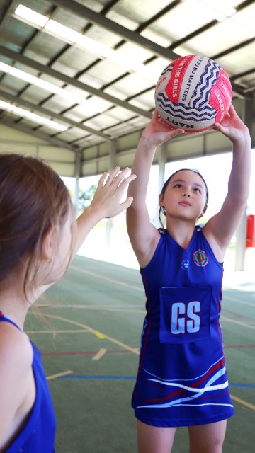 Student attempting a netball shot during an indoor game, highlighting participation in sport, skill development and confidence through physical activity